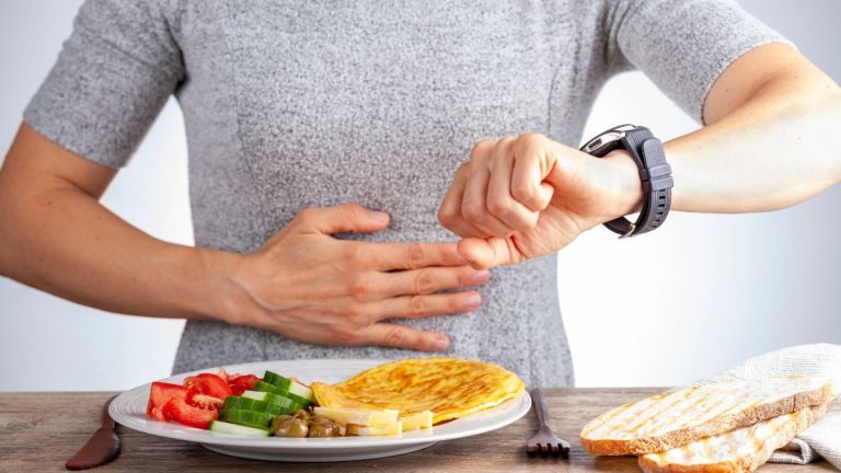personne qui regarde sa montre devant une assiette de nourriture