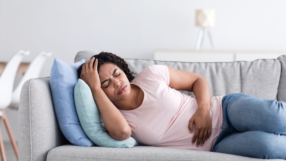 femme avec douleurs tete et ventre allonge sur canape