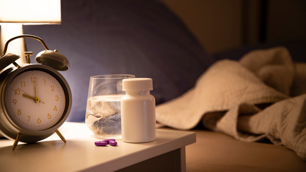 flacon de somniferes et reveil sur table de nuit