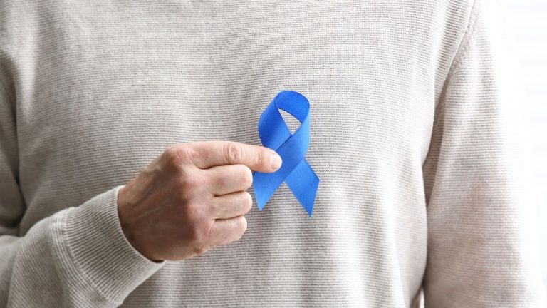 un homme tient un noeud bleu cancer colorectal